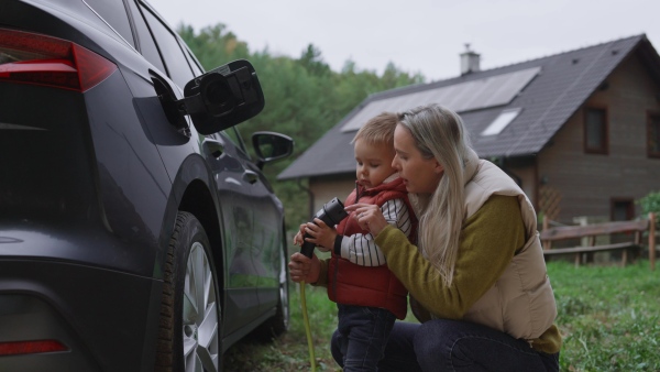 A young mom and boy charging family electric car. EV home charging station.