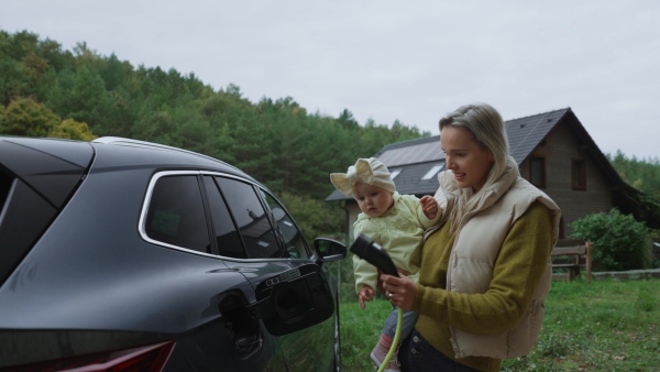 A young mom and girl charging family electric car. EV home charging station.