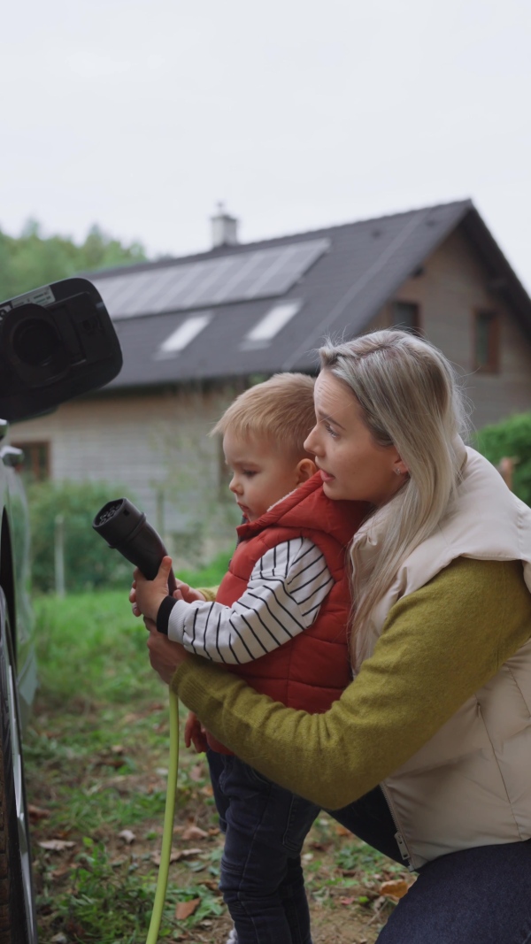 A young mom and boy charging family electric car. EV home charging station.