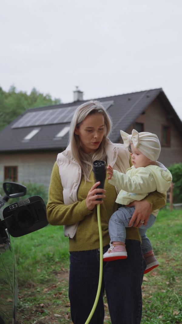 A young mom and girl charging family electric car. EV home charging station.