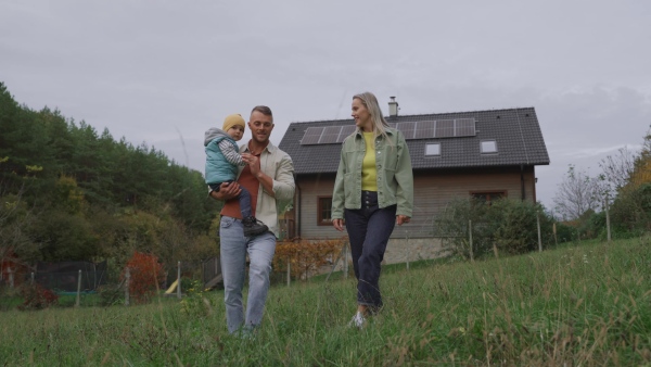 Family house with rooftop solar panels. Young family in front of their solar-powered home.