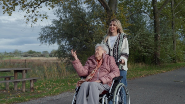 An autumn walk with wheelchair, disabled senior woman and her daughter spending a chilly, windy day outdoors in nature.