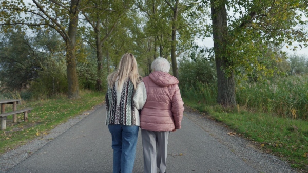 Autumn walk, rear view of a senior woman and her daughter spending a chilly, windy day outdoors in nature.