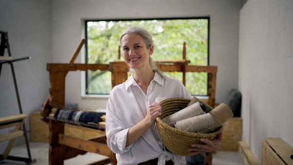 A woman holding basket full of threads in her weaving workshop. Sustainable business, using recycled materials in fashion.