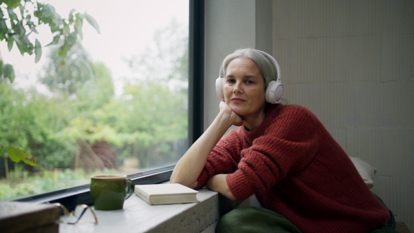 Woman taking a break, reading book by window and drinking warm herbal tea.