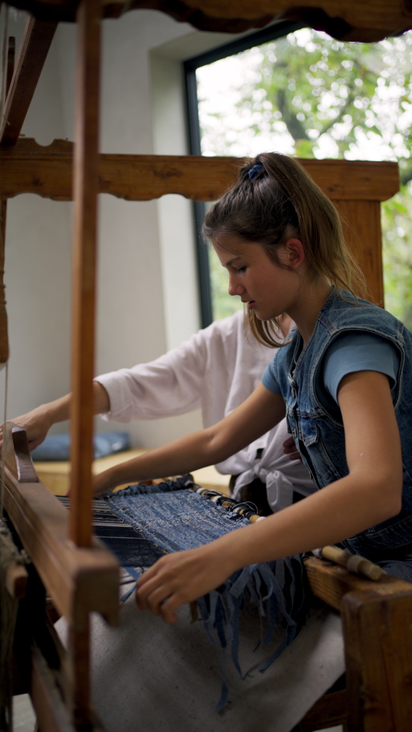 A ,other and daughter working on wooden loom, weaving. Sustainable business, using recycled materials in fashion.