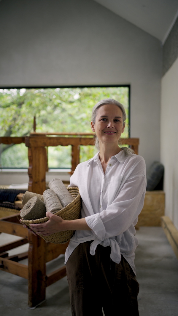 A woman holding basket full of threads in her weaving workshop. Sustainable business, using recycled materials in fashion.