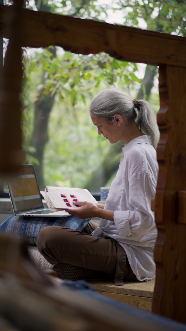 A businesswoman in weaving workshop, working on laptop. Sustainable business, using recycled materials in fashion.