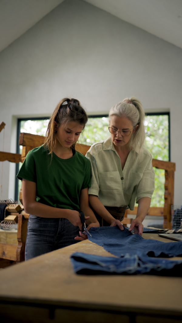 Mom teaching her daughter how to prepare material for weaving. Working together in family workshop. Sustainable business, using recycled materials in fashion.