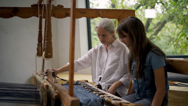 A mother and daughter working on wooden loom, weaving. Sustainable business, using recycled materials in fashion.