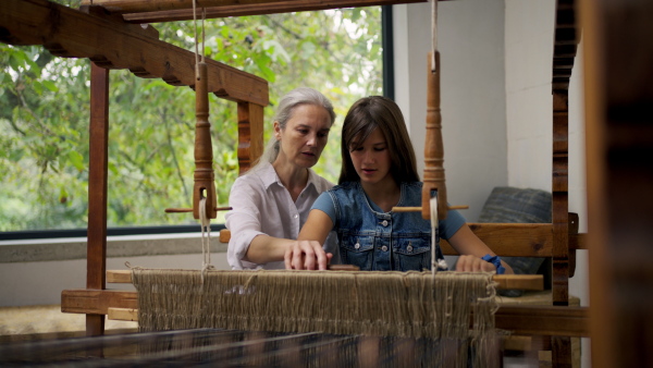 A mother and daughter working on wooden loom, weaving. Sustainable business, using recycled materials in fashion.