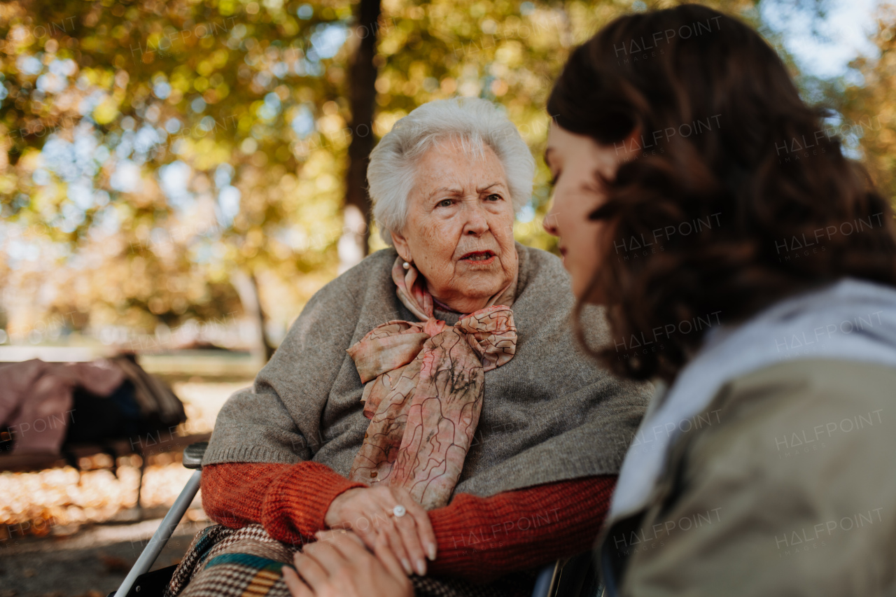 Disabled elderly woman in wheelchair holding hands with her caregiver and talking.