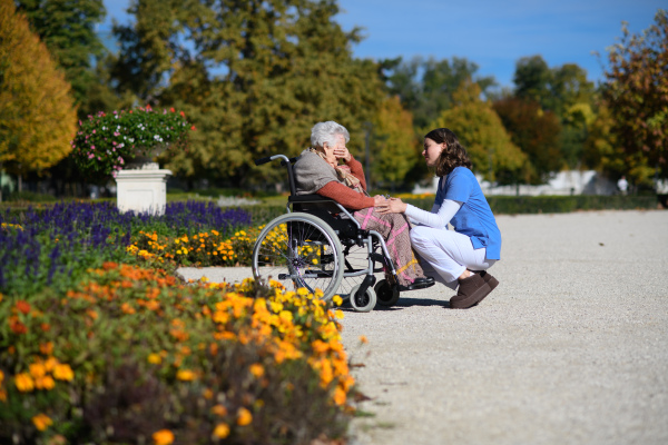 Disabled elderly woman in wheelchair holding hands with her nurse and talking about her problems.