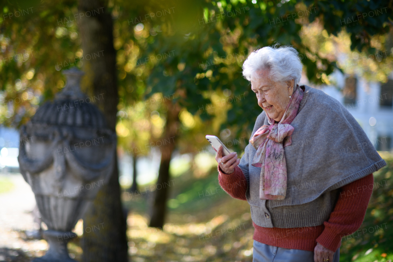 Elderly woman in the park, holding smartphone and reading message.