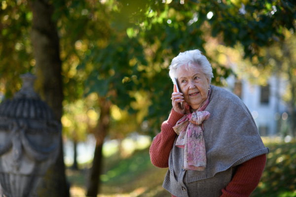 Elderly woman in the park, holding a smartphone and phone calling.