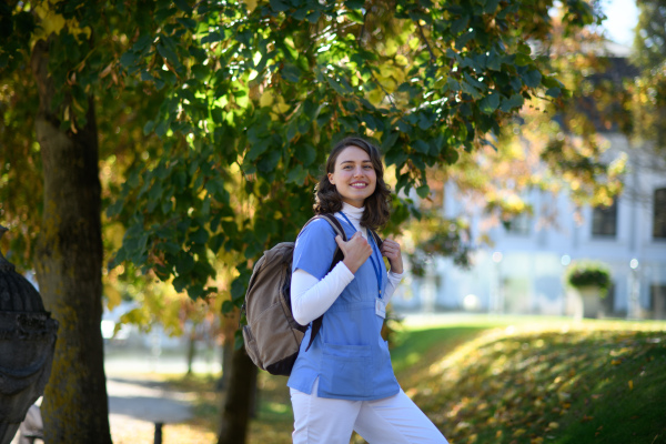 Beautiful nurse walking to work with backpack on her back. Autumn walk from hospital to home for young female healthcare worker.