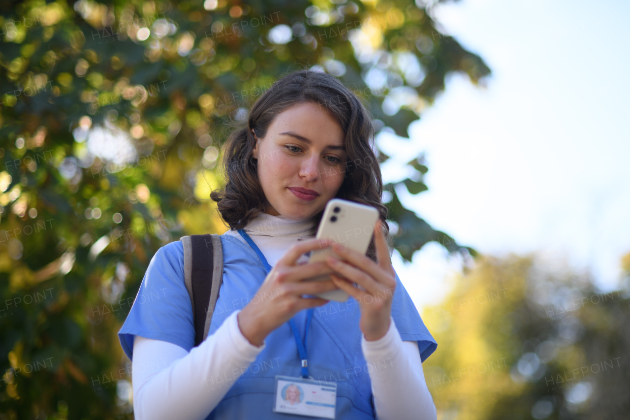 Beautiful nurse in uniform holding smartphone in hands, scrolling, looking at device screen