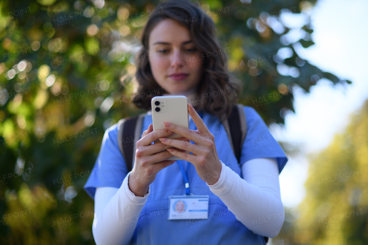 Beautiful nurse in uniform holding smartphone in hands, scrolling, looking at device screen