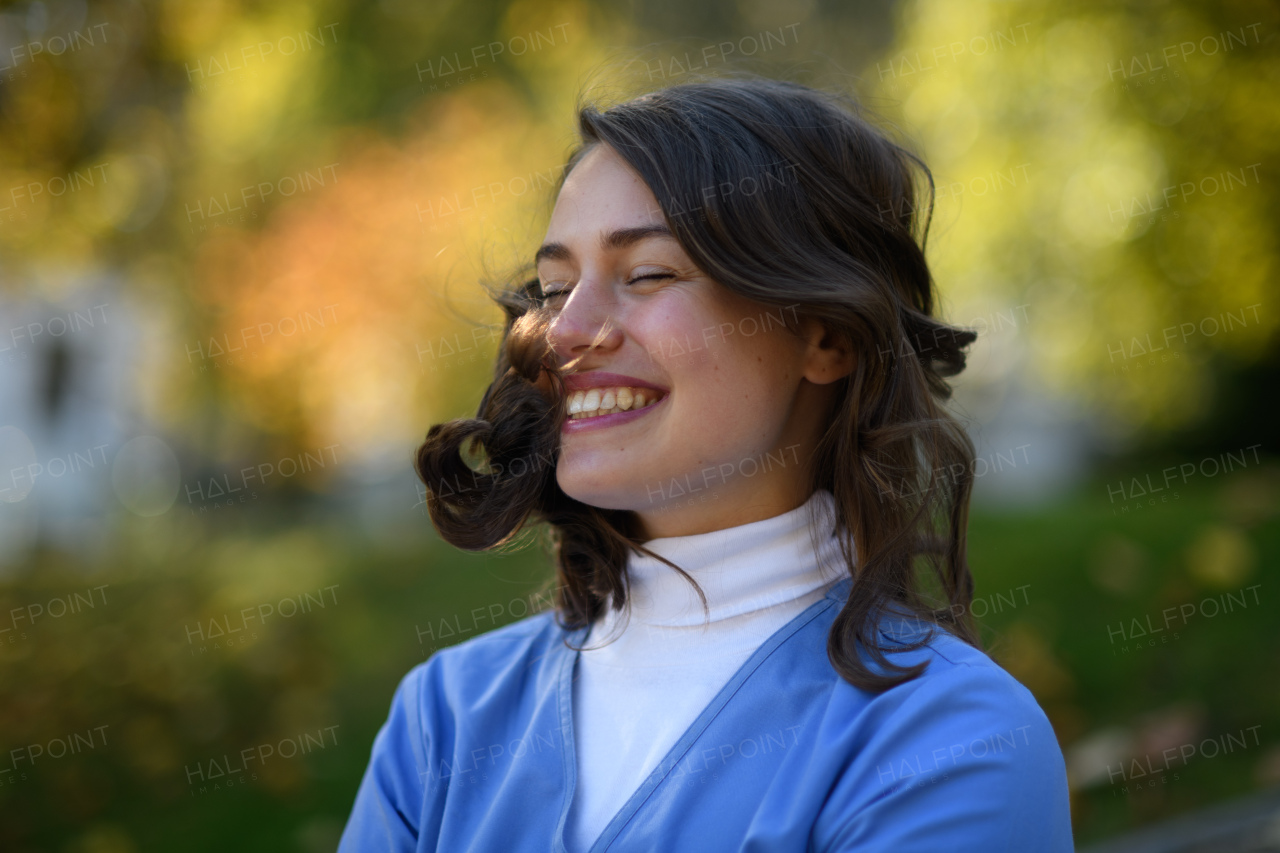 Portrait of beautiful nurse with closed eyes and hair in face, standing outdoors