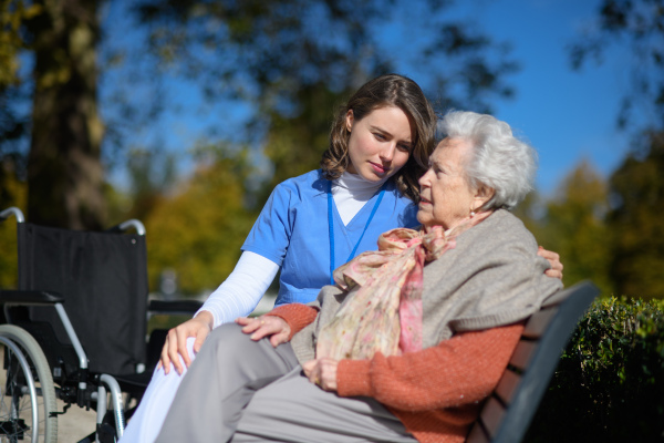 Elderly woman talking with therapist in the park, sitting on bench. Outdoor therapy for senior woman in nursing home.