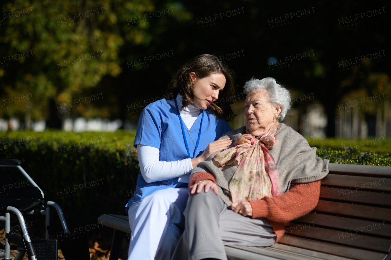 Elderly woman talking with therapist in the park, sitting on bench. Outdoor therapy for senior woman in nursing home.