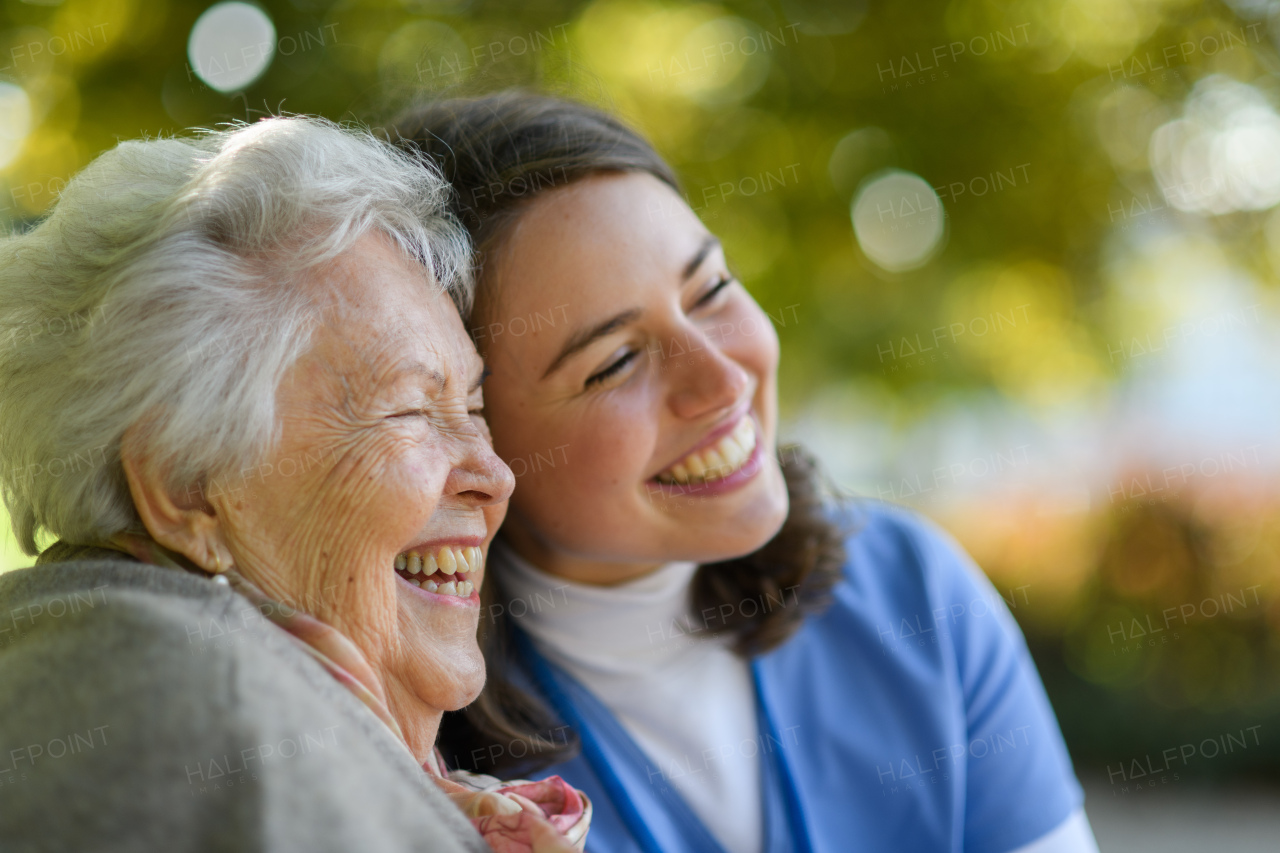 Portrait of nurse and elderly woman in autmn park. Young caregiver spending time with female senior patient.