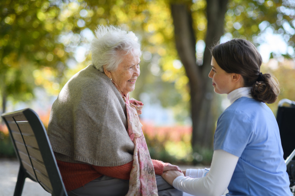 Disabled elderly woman in wheelchair holding hands with her nurse and talking about her problems.