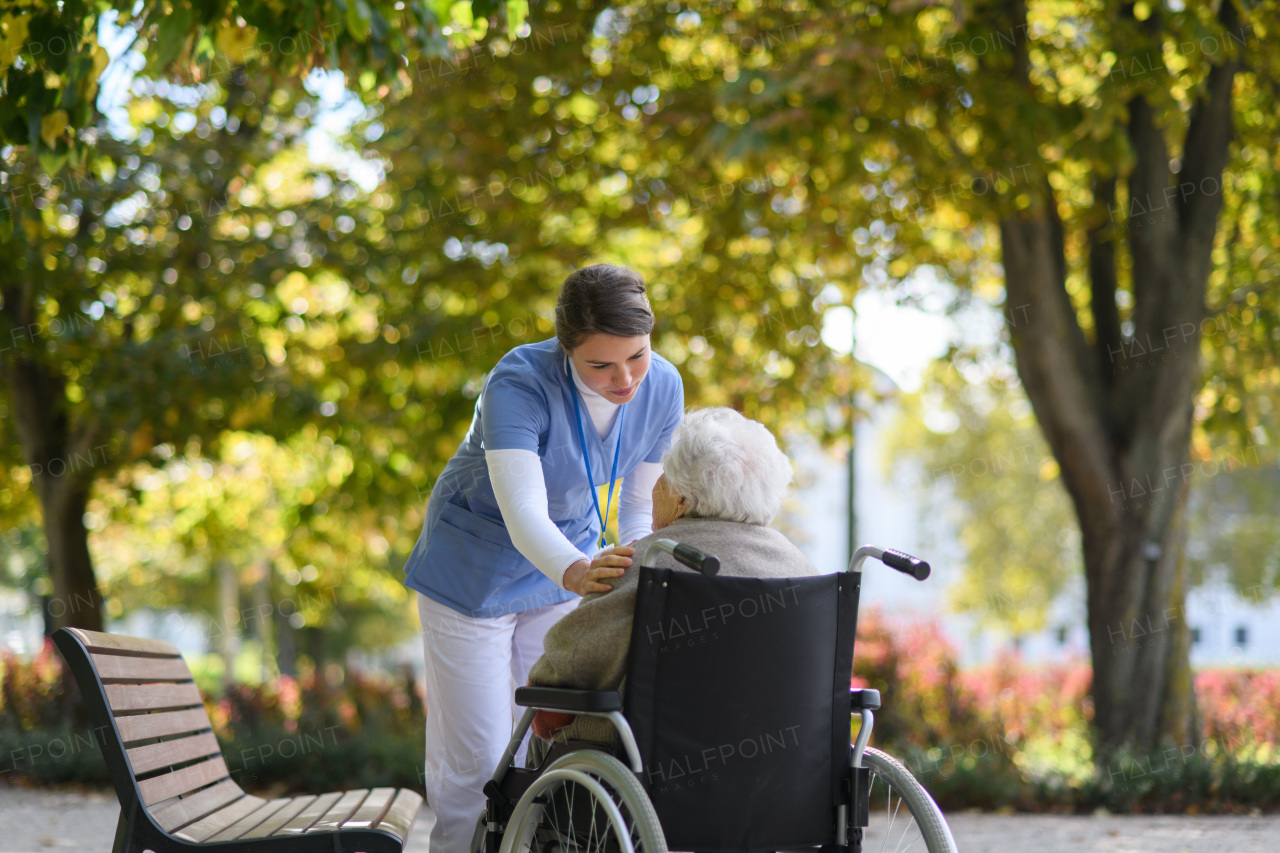 Disabled elderly woman in wheelchair talking with nurse, sharing her problems with female caregiver.