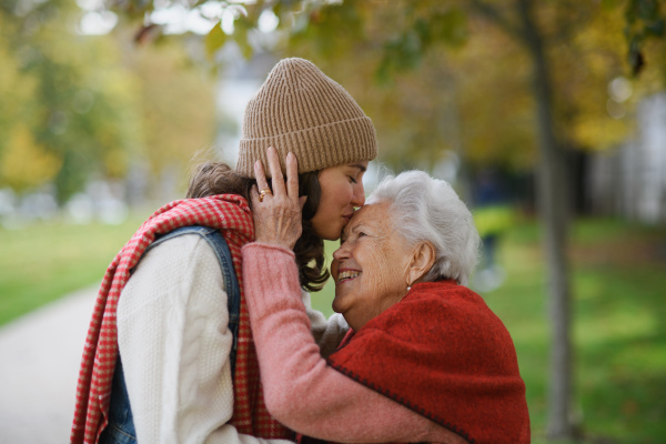 Portrait of granddaughter on an autumn walk in the park with her grandmother, kissing her forehead.