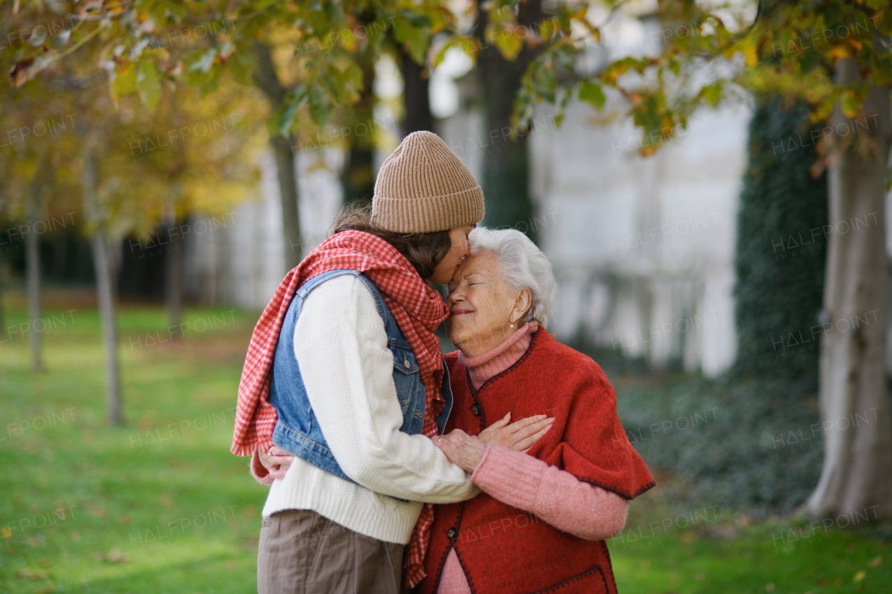 Portrait of a granddaughter kissing grandmother on forehead during autumn walk in the park.