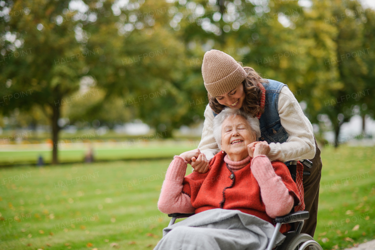 Granddaughter on an autumn walk in the park with her grandmother, pushing her in wheelchair.