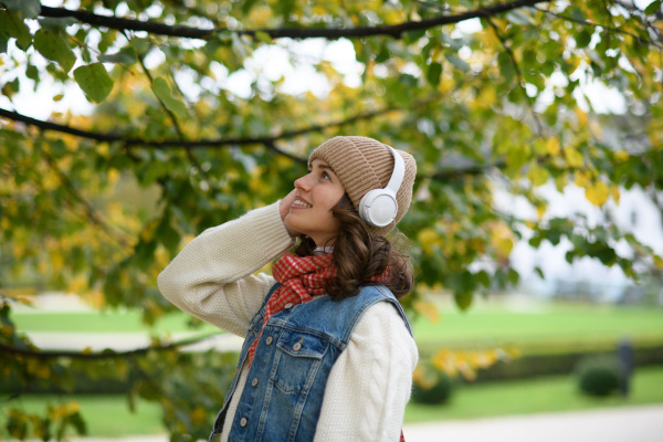 Beautiful young woman on a walk in the autumn park, listening to music and enjoying peaceful moment for herself.