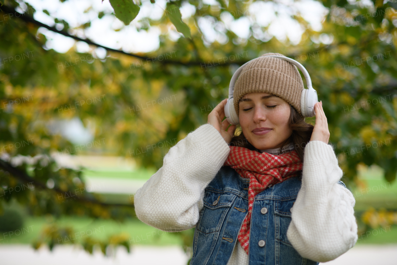 Beautiful young woman on a walk in the autumn park, listening to music and enjoying peaceful moment for herself.