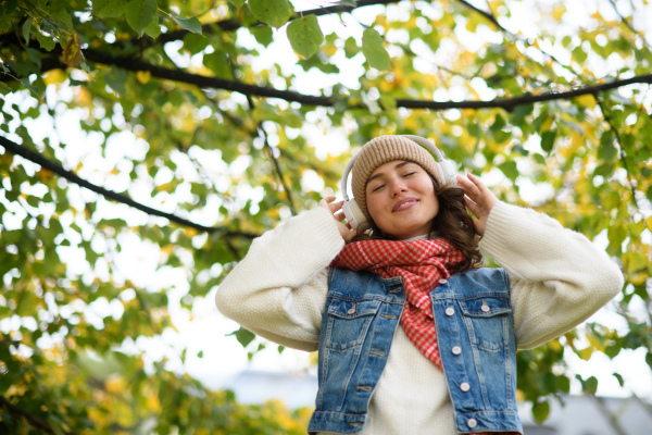 Beautiful young woman on a walk in the autumn park, listening to music and enjoying peaceful moment for herself.