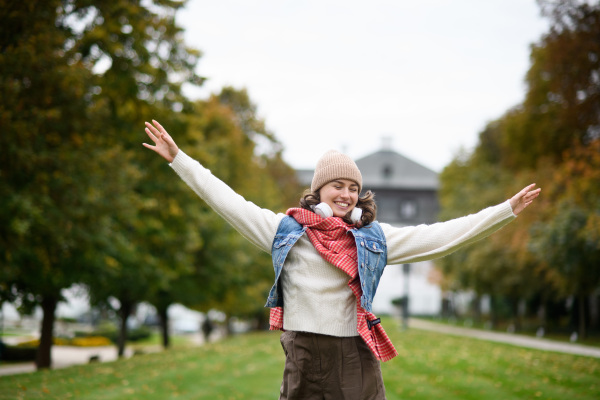 Beautiful woman in the middle of autumn park, standing with outstretched arms, enjoying seasonal weather around her.