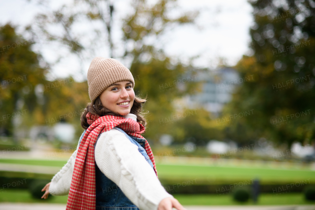 Beautiful woman in the middle of autumn park, standing with outstretched arms, enjoying seasonal weather around her.