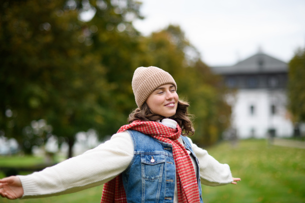 Beautiful woman in the middle of autumn park, standing with outstretched arms, enjoying seasonal weather around her.