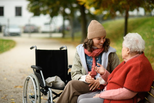 Granddaughter and grandmother sitting on bench in autumn park, talking.