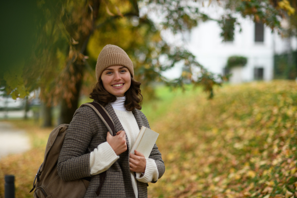 Female university student walking from lecture to her dorm, passing through the autumn park.