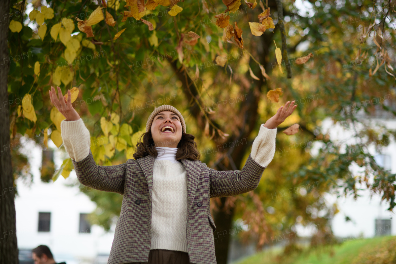 Portrait of a beautiful woman in the middle of autumn park, throwing leaves in the air. She smiles and looking at camera