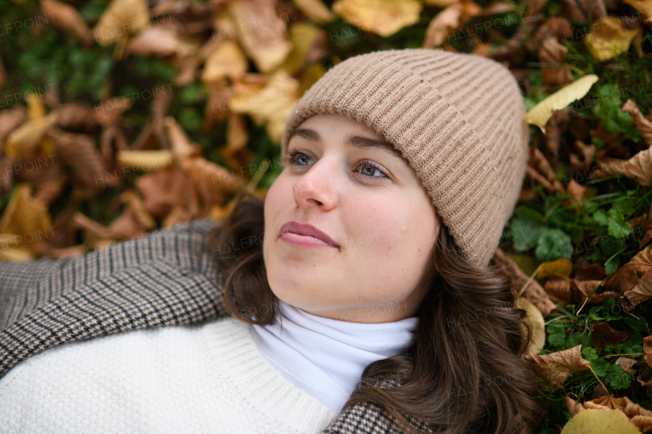 Portrait of beautiful woman lying in fallen autumn leaves on the lawn. She smiles and looking at camera.