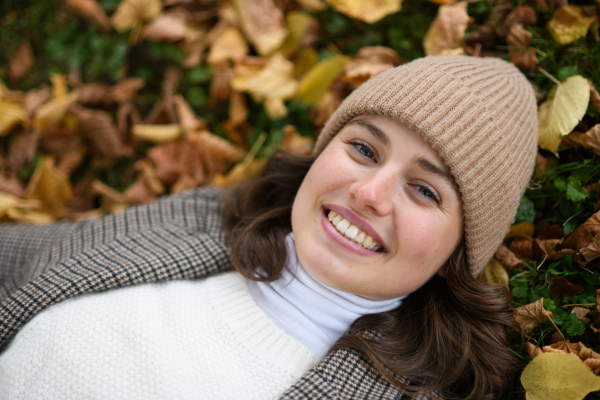 Portrait of beautiful woman lying in fallen autumn leaves on the lawn. She smiles and looking at camera.