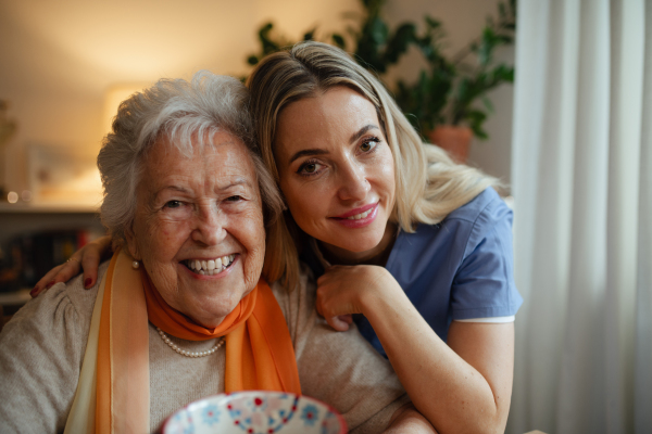 Portrait of smiling nurse and senior patient, hugging her during visit at home.