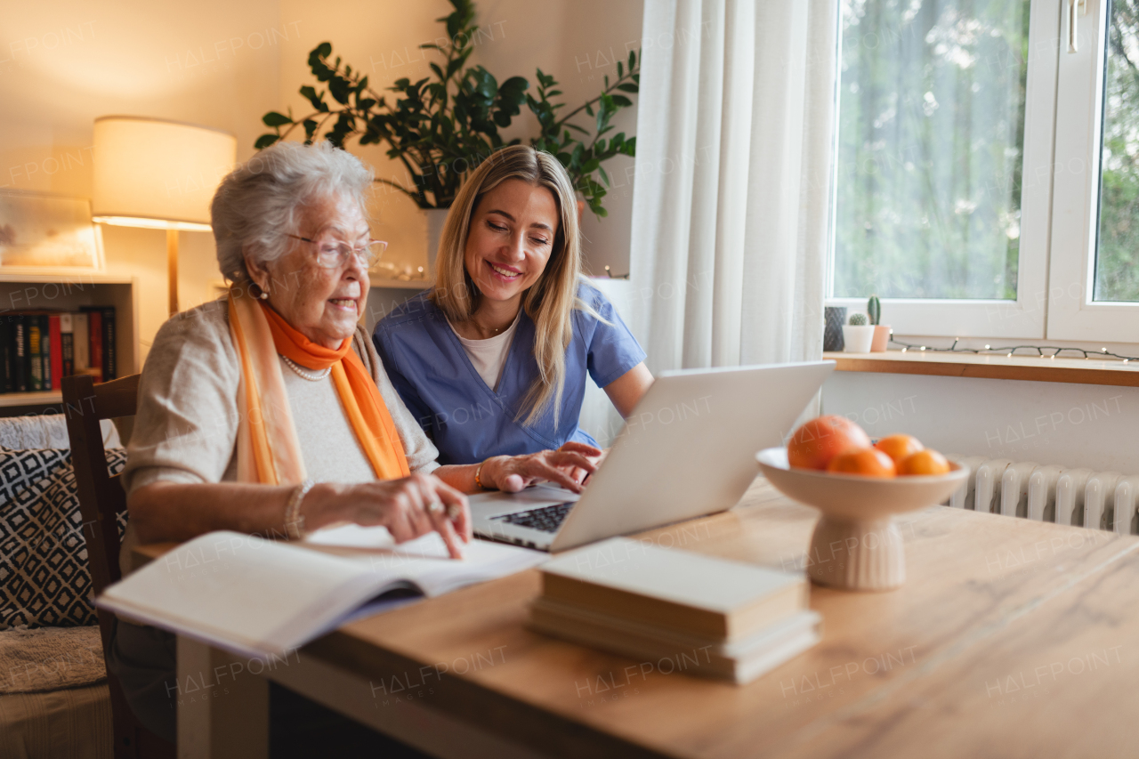 Social worker helping elderly lady with managing her finances and teaching her to use online banking on laptop.