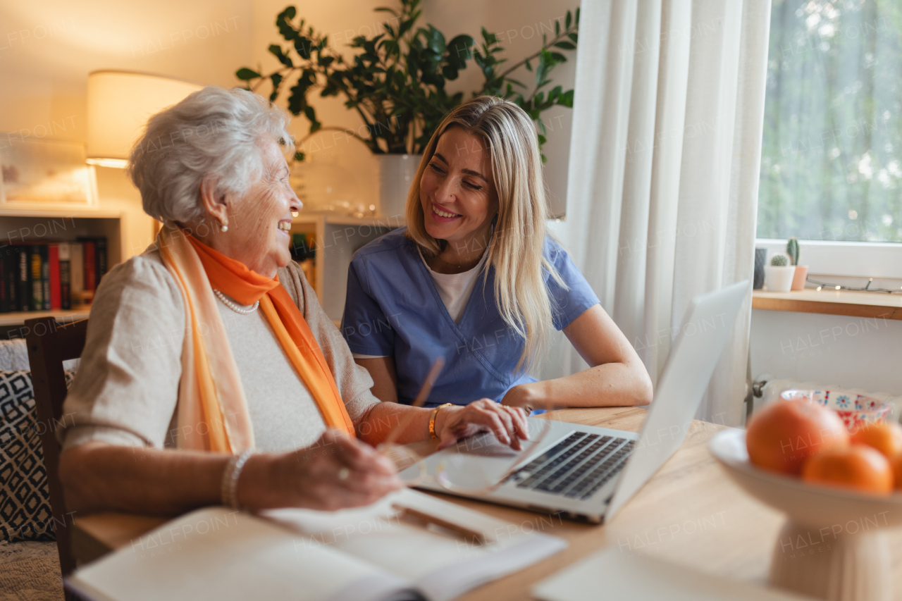 Social worker helping elderly lady with managing her finances and teaching her to use online banking on laptop.