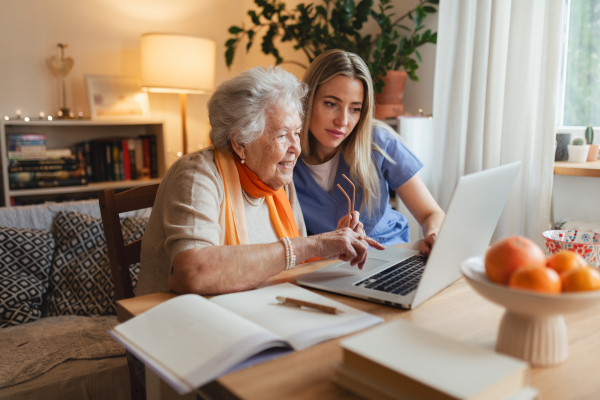 Social worker helping elderly lady with managing her finances and teaching her to use online banking on laptop.