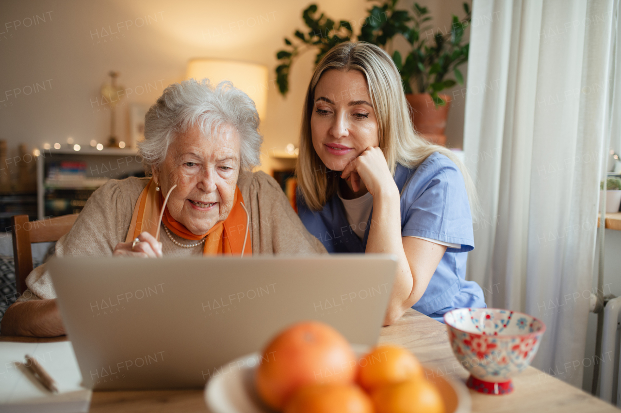 Elderly woman learning how to work with laptop, social worker helping her. Concept of managing finances and online banking for seniors.