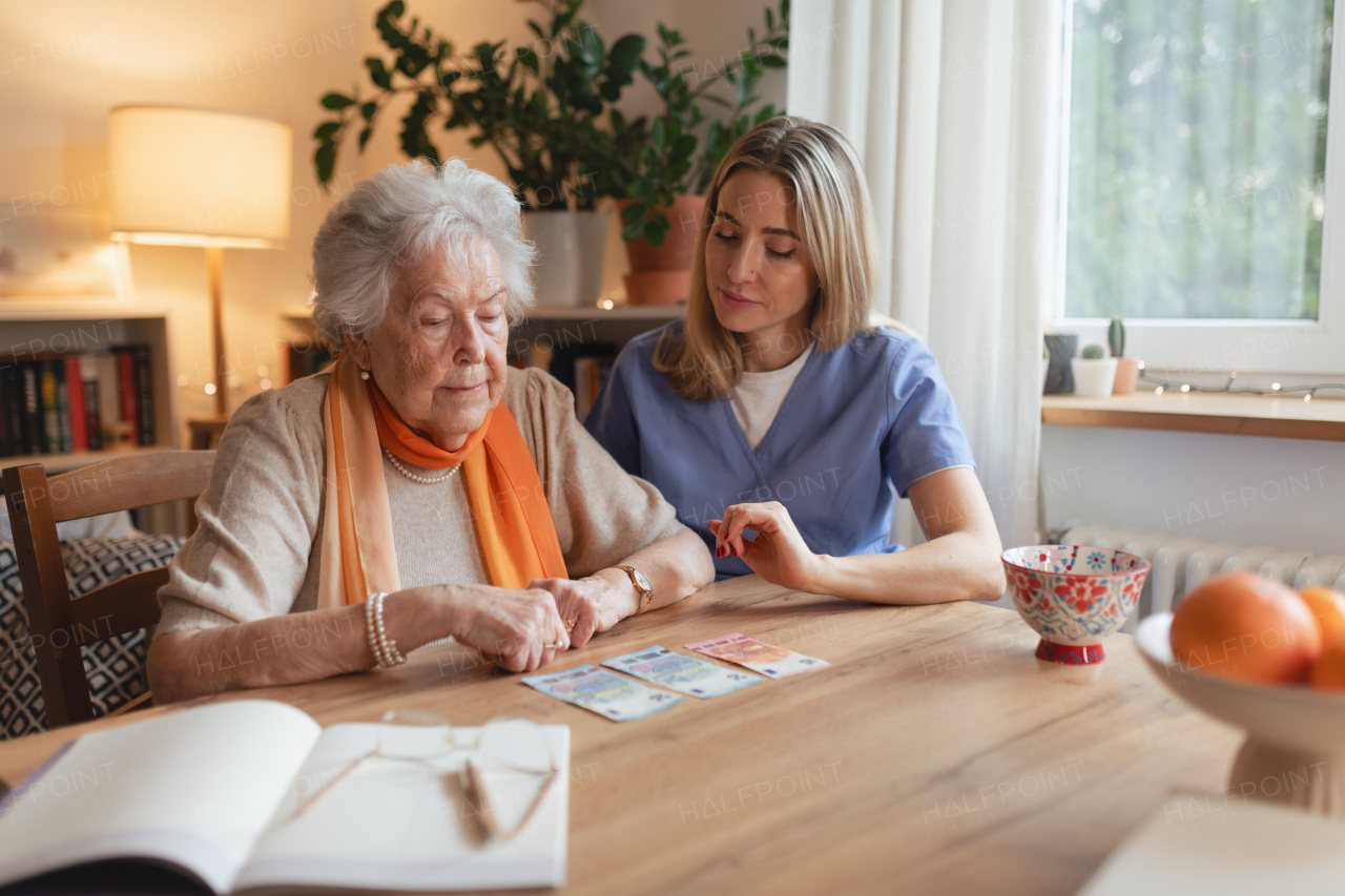 Social worker helping elderly lady with managing her finances and counting banknotes.