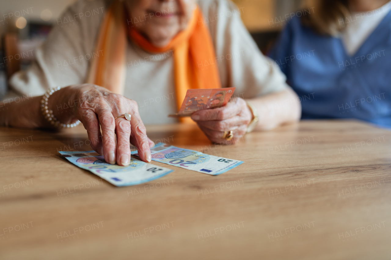 Social worker helping elderly lady with managing her finances and counting banknotes.