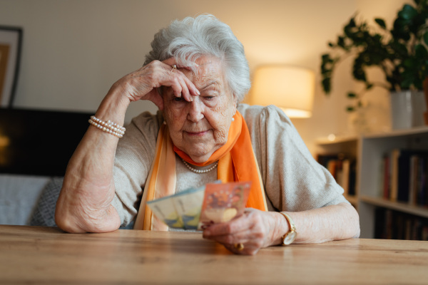 Elderly woman looking sadly at few banknotes in her hand. Concept of financial struggles for seniors.